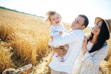 Mutlu bir yaz yürüyüşü yapan aile, anne, baba ve çocuk buğday tarlasında yürüyor ve gün batımında güzel doğanın tadını çıkarıyor. Yüksek kalite fotoğraf