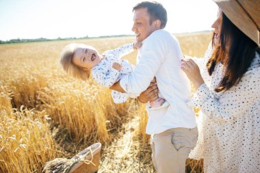 Mutlu bir yaz yürüyüşü yapan aile, anne, baba ve çocuk buğday tarlasında yürüyor ve gün batımında güzel doğanın tadını çıkarıyor. Yüksek kalite fotoğraf