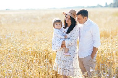 Mutlu bir çocukluk, aile buğday tarlasında yürüyor. Anne, baba ve küçük kız birlikte dışarıda vakit geçiriyorlar. Ebeveynler ve çocuklar yaz otlaklarında oynuyorlar. Yüksek kalite fotoğraf