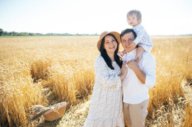 Mutlu bir yaz yürüyüşü yapan aile, anne, baba ve çocuk buğday tarlasında yürüyor ve gün batımında güzel doğanın tadını çıkarıyor. Yüksek kalite fotoğraf