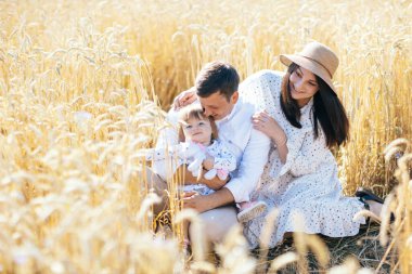 Mutlu bir çocukluk, aile buğday tarlasında yürüyor. Anne, baba ve küçük kız birlikte dışarıda vakit geçiriyorlar. Ebeveynler ve çocuklar yaz otlaklarında oynuyorlar. Yüksek kalite fotoğraf