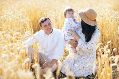 Mutlu bir çocukluk, aile buğday tarlasında yürüyor. Anne, baba ve küçük kız birlikte dışarıda vakit geçiriyorlar. Ebeveynler ve çocuklar yaz otlaklarında oynuyorlar. Yüksek kalite fotoğraf