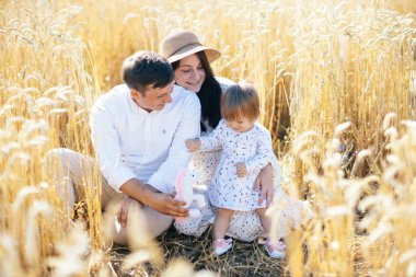Mutlu bir çocukluk, aile buğday tarlasında yürüyor. Anne, baba ve küçük kız birlikte dışarıda vakit geçiriyorlar. Ebeveynler ve çocuklar yaz otlaklarında oynuyorlar. Yüksek kalite fotoğraf