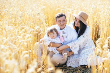 Mutlu bir çocukluk, aile buğday tarlasında yürüyor. Anne, baba ve küçük kız birlikte dışarıda vakit geçiriyorlar. Ebeveynler ve çocuklar yaz otlaklarında oynuyorlar. Yüksek kalite fotoğraf