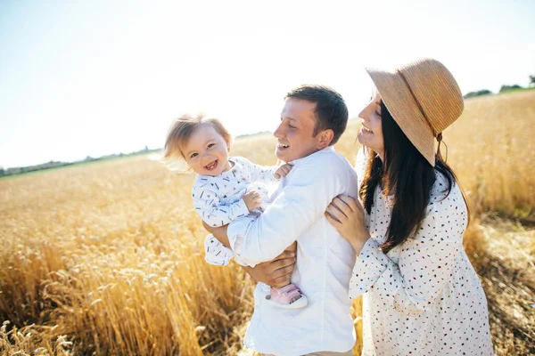 Mutlu bir yaz yürüyüşü yapan aile, anne, baba ve çocuk buğday tarlasında yürüyor ve gün batımında güzel doğanın tadını çıkarıyor. Yüksek kalite fotoğraf