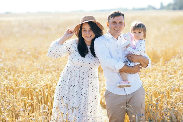 Mutlu bir yaz yürüyüşü yapan aile, anne, baba ve çocuk buğday tarlasında yürüyor ve gün batımında güzel doğanın tadını çıkarıyor. Yüksek kalite fotoğraf