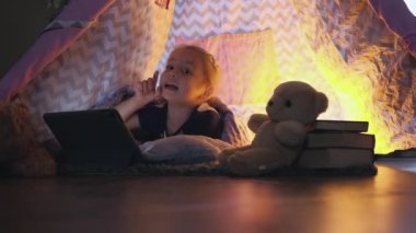 Akşam oynayan küçük kız tablette, çadırda çizgi film izliyor. Yüksek kaliteli FullHD görüntüler