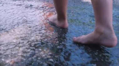 Kaldırımdaki su birikintisi. Yağmur damlaları suya düşer. Yavru çıplak ayaklar havuzda su püskürterek koşuyor. Yüksek kaliteli FullHD görüntüler