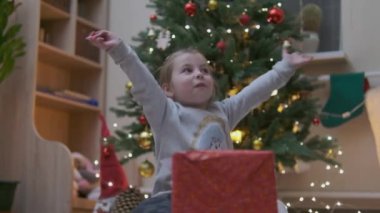 Heyecanlı küçük meraklı kız gülümsüyor, Noel hediyelerini açıyor. Çok güzel dekore edilmiş yılbaşı ağacı ve ışıkları ve feneri olan bir ev. Yüksek kalite fotoğraf