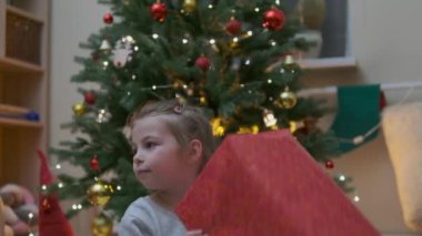 Heyecanlı küçük meraklı kız gülümsüyor, Noel hediyelerini açıyor. Çok güzel dekore edilmiş yılbaşı ağacı ve ışıkları ve feneri olan bir ev. Yüksek kalite fotoğraf