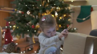 Heyecanlı küçük meraklı kız gülümsüyor, Noel hediyelerini açıyor. Çok güzel dekore edilmiş yılbaşı ağacı ve ışıkları ve feneri olan bir ev. Yüksek kalite fotoğraf
