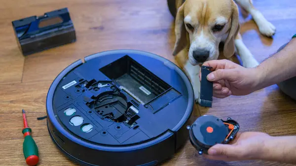 Caucasian young man with beagle dog doing vacuum cleaner robot maintenance. Male starts automatic vacuum cleaner. Robot vacuum cleaner repair. High quality photo