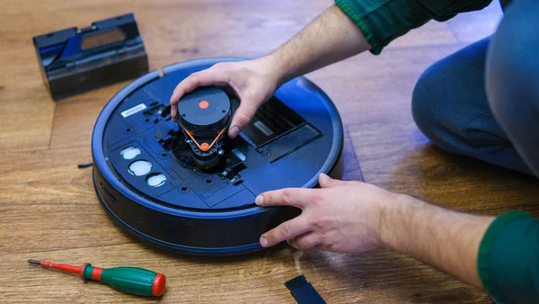 Robot vacuum cleaner repair. Man fixing robot vacuum cleaner DIY at home on the floor. Robotic vacuum cleaner maintenance and service. Smart device for easy housework. New tech for households. High