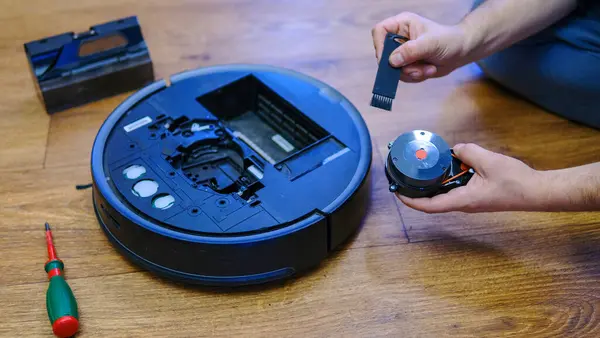 Housework and technology concept. Maintenance and service of robot vacuum cleaner. Cleaning, repair, replacement of parts. Man repairing robot cleaner at home. Smart home functions, fully automated