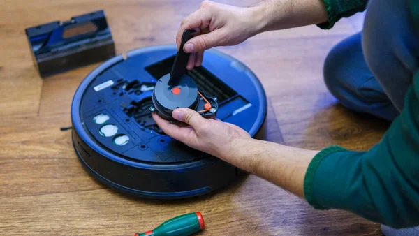 Caucasian young man doing vacuum cleaner robot maintenance. Male starts automatic vacuum cleaner. Robot vacuum cleaner repair. High quality photo