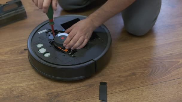 ロボット掃除機の修理 床の自宅でロボット掃除機Diyを固定する男 ロボット掃除機のメンテナンスとサービス 容易な家事のためのスマートな装置 世帯のための新しい技術 — ストック動画