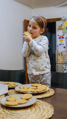 Sevimli küçük kız, annesi Noel yemeğinden önce dekore ederken ev yapımı zencefilli kurabiyeleri tadıyor. Yüksek kalite fotoğraf