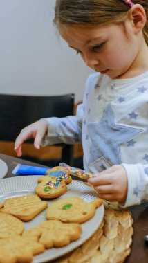 Küçük bir kız mutfak masasında zencefilli kurabiye süslüyor. Noel için hazırlanıyorum. Yüksek kalite fotoğraf