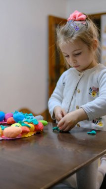 Paskalya yumurtalarıyla oynayan küçük bir kız boncuklarla hamur süsleme oyunu oynuyor. Paskalya için şirin çocuk el sanatları. Çocuklar için Tatil Sanatı Etkinliği. Güzel motor beceriler, yaratıcılık ve hobi. Yüksek kalite