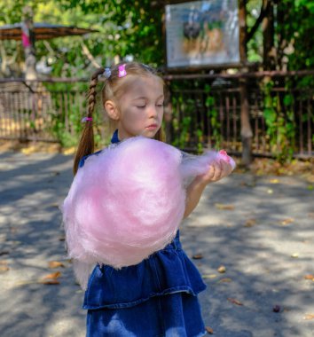 Yeşil duvar arka planında pembe pamuk şekerli küçük bir kızın portresi. Eğlence parkına gidip eğlenen mutlu çocuklar. Yüksek kaliteli FullHD görüntüler