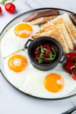 Izgara sosisli kahvaltı, çırpılmış yumurta, kiraz domatesleri ve tost.