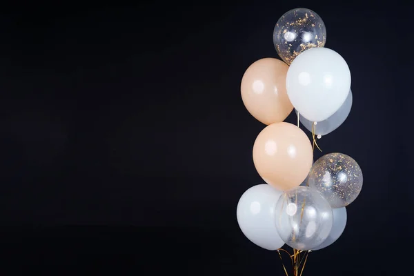 A bunch of balloons in white, beige and transparent colors on a dark background with space for an inscription. High quality photo