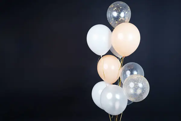 On a black background, balloons of light shades - white, beige, transparent - are flying. Space for text. High quality photo