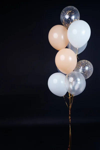 A bunch of balloons in white, beige and transparent colors on a dark background with space for an inscription. High quality photo