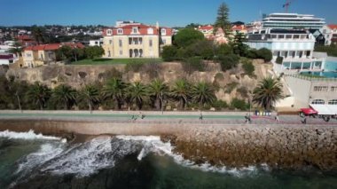Portekiz Riveira 'sına çarpan dalgalarla Cascais' den Estoril 'e gezen insanların yan panoları.