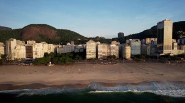 Aerial drone view panning Avenida Atlantica in Copacabana, Rio de Janeiro, Brazil at dusk with waves crashing underneath