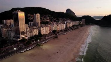 Aerial drone backwards view over Leme Beach in the Copacabana District, Rio de Janeiro, Brazil at dusk with Sugarloaf mountain visible in background