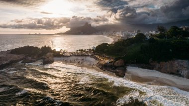 Aerial drone view above Praia do Diabo, Arpoador and Ipanema Beaches in Rio de Janeiro, Brazil on a cloudy day with many Cariocas enjoying the beaches