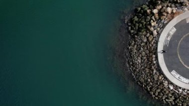 Aerial top down view of man at end of pier next to sea