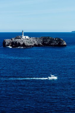 Magdalena Yarımadası, Santander, İspanya 'dan küçük bir tekne yelkenlisi ve arka planda 19. yüzyıldan kalma deniz feneriyle birlikte Mouro Adası manzarası.