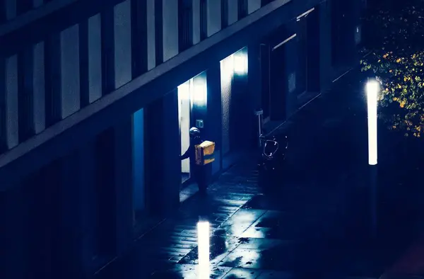 Food delivery person outside an apartment building at night.