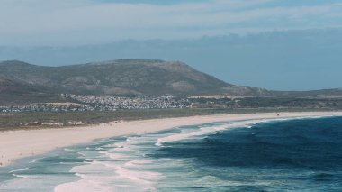 The tranquil scene captures the untouched beauty of Noordhoek Beach as the gentle waves wash over the pristine white sands. The backdrop of the rolling hills complements the peaceful beach, highlighting the natural splendor of South Africas coastline clipart