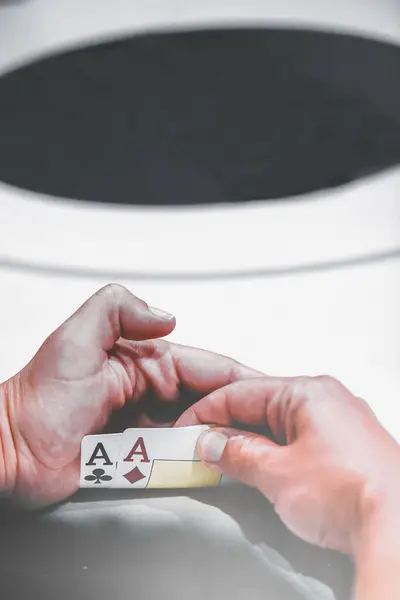 Close-up view of a poker players hands covertly holding a pair of aces, the strongest starting hand in Texas Holdem. The player seems to be in a decisive moment at the casino table, with poker chips visible in the background.