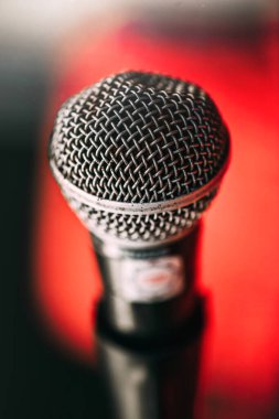 Detaylı bir makro çekim. Mikrofonlar, karmaşık tel örgüler ve dokular, canlı kırmızı bir zemin üzerine kurulmuş, bir akşam konserinin enerjisini vurguluyor..