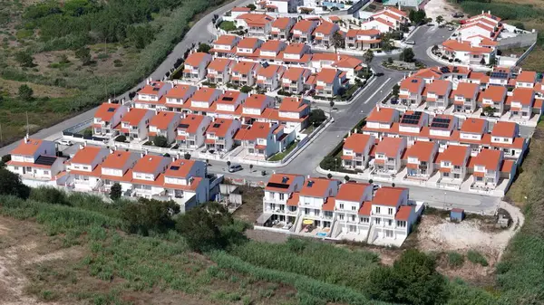 stock image A sprawling residential community features rows of houses, each with distinctive red roofs, nestled among lush greenery. Conveniently located near a winding road