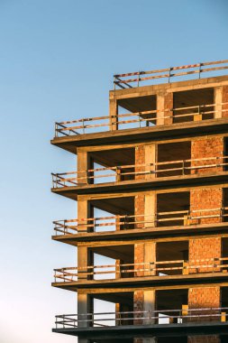 Kısmen inşa edilmiş bir bina, akşam saatlerinde içinde güvenlik bariyerleri bulunan çiğ tuğla ve betonu gösteriyor..