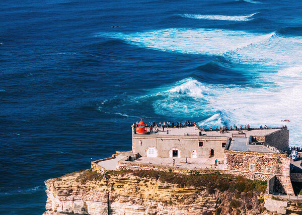 Aerial drone view of people admiring the giant waves from the lighthouse at Nazare, Portugal