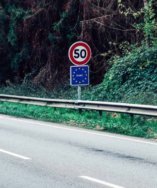 Speed limit sign indicating 50 km/h on a rural road in France surrounded by greenery and trees during daytime clipart