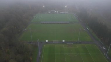 Gri ve yağmurlu bir günde yapılan futbol antrenmanına genel bir bakış. Oyuncular aktif olarak antrenman yaparken, koçlar saha kenarından izliyor.