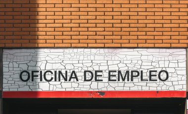 Employment office sign in Spanish on a brick wall indicating job services available for local community members clipart