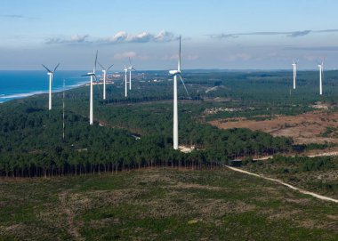 Manzara, kıyı şeridi boyunca uzanan yenilenebilir enerji çabalarını ön plana çıkaran yoğun bir ormanla çevrili birden fazla rüzgar türbini gösteriyor. Portekiz 'de Nazare' de yakalandı.