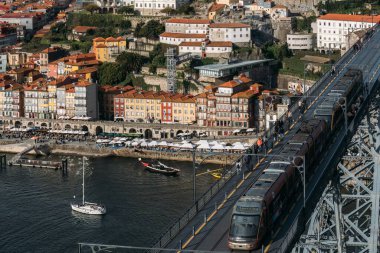 Porto, Portugal - December 15, 2024: Vibrant Ribeira waterfront of Porto showcasing colorful buildings and lively river activities during a sunny day with Luis I Bridge visible clipart