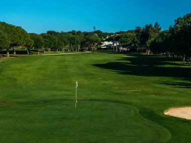 İyi korunan bir golf sahasında Portekiz 'in Algarve şehrinde açık mavi gökyüzü altında canlı yeşil bir çim yolu sergileniyor.