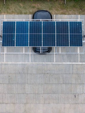 Photovoltaic solar panels are installed above a black parked vehicle, showcasing the integration of renewable energy technology in an urban environment clipart