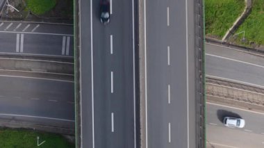 Hava görüntüsü, araçların gün ışığında çeşitli şeritlerden geçtiği bir kavşak yakalar. Manzara trafik ve yol yapısının akışını vurgular
