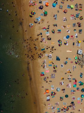 Portekiz 'in Cascais kentinde bir yaz öğleden sonrası boyunca renkli şemsiyeler ve güneş banyosu yapan kalabalık bir plajın aşağı bakan hava aracı görüntüsü.